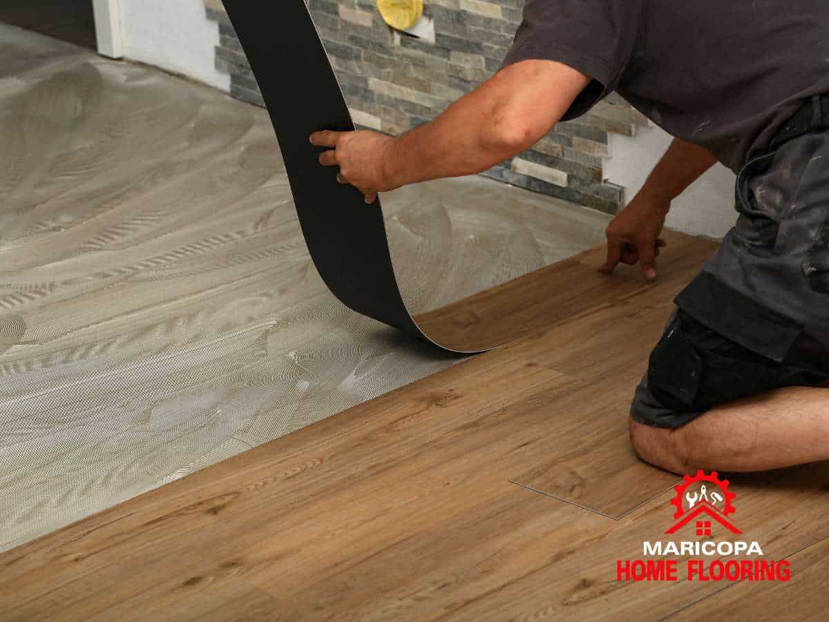 Contractor installing vinyl flooring in a home using adhesive and planks